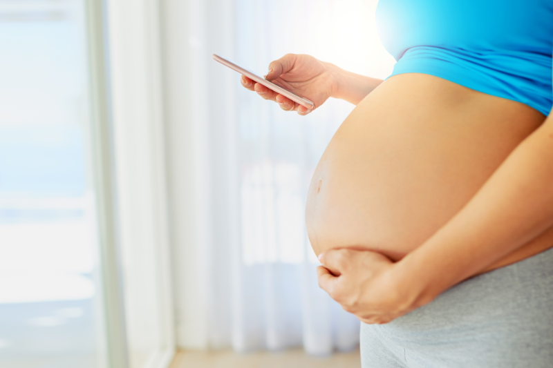 A pregnant woman embracing her belly while searching on her phone
